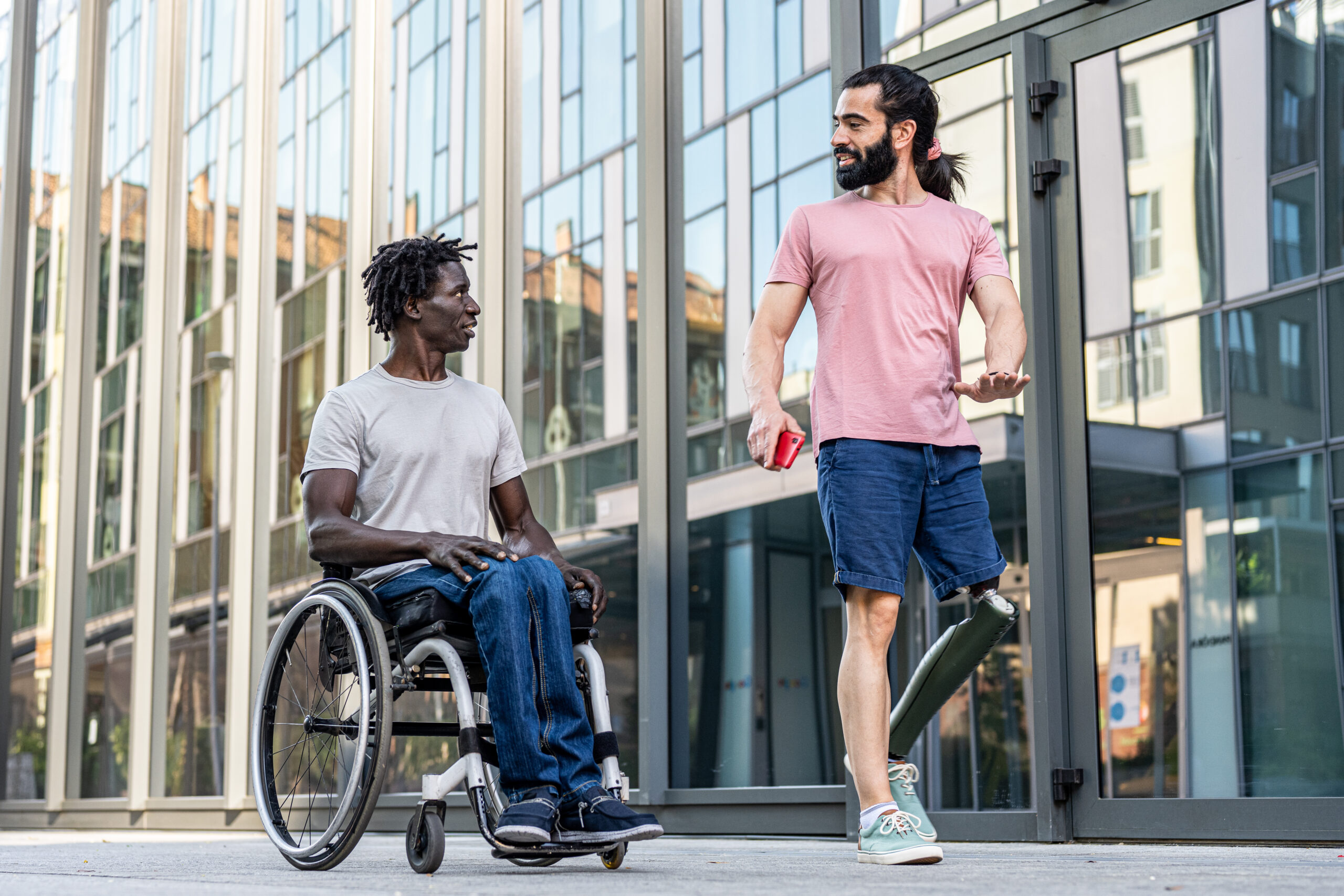 Two diverse friends having some disabilities walking in the city, people on wheel chair and artificial limb lifestyle